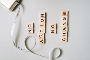 Scrabble tiles form motivational message ‘No Action No Change’ with a measuring tape.